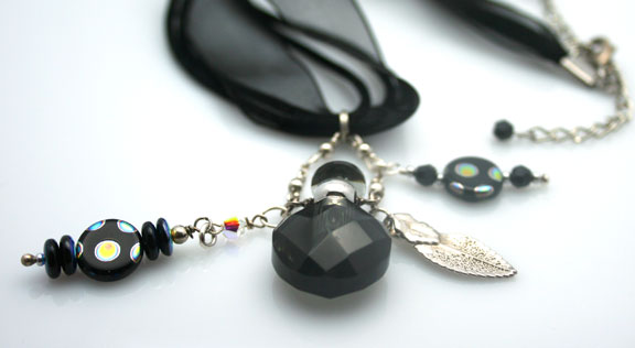 Close-up photo of the black, faceted, mini perfume bottle and beads on a black ribbon