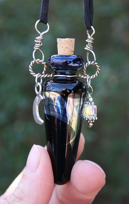closeup of lampwork poison bottle with dangle charms