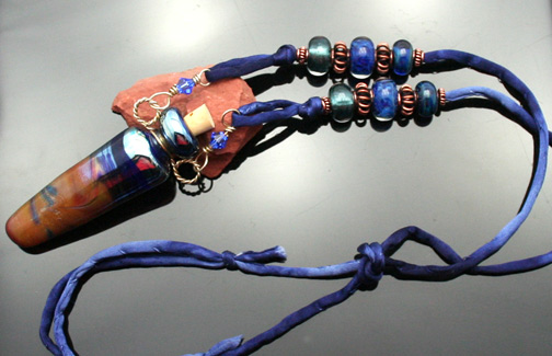 Gorgeous aromatherapy pendant featuring swirling earth tones, deep blue and silver accents. Finishing the piece is a hand-sewn denim silk cord and copper beads.
