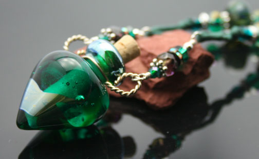 Dark green glass aromatherapy bottle with swirls of silver hangs on a mint green silk cord with glass and silver beads